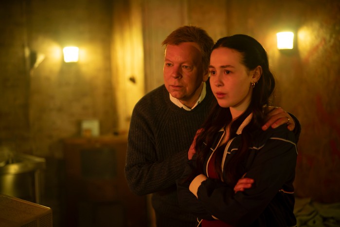 475579,Inside No. 9 S9 Jason puts his arm around his daughter's shoulders in a dimly lit escape room environment