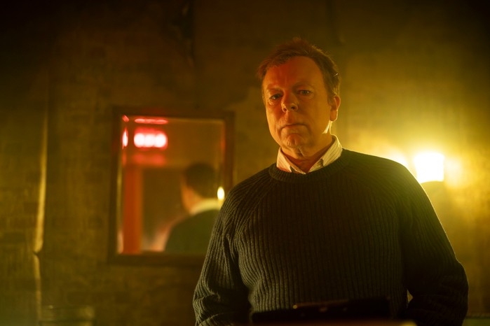 475585,Inside No. 9 S9 Jason in a dimly lit escape room with a mirror on the wall behind him