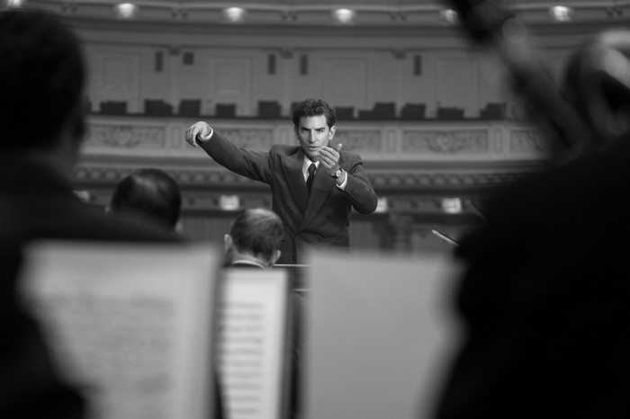 Bradley Cooper as Leonard Bernstein in Maestro Bradley Cooper as Leonard Bernstein in Maestro wearing a suit, conducting an orchestra