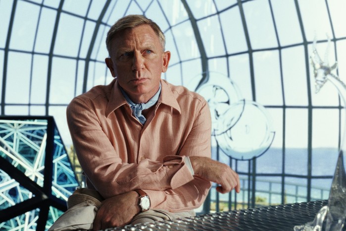 Daniel Craig as Benoit Blanc in Glass Onion Daniel Craig as Benoit Blanc in Glass Onion in an orange shirt sat in a glass building