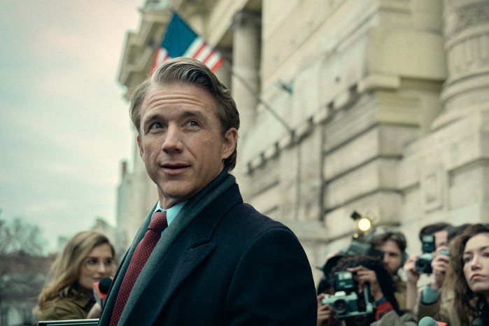 Eric Season 1 Jeff Hephner as Costello in Eric standing outside in a suit and coat and being surrounded by paparazzi.