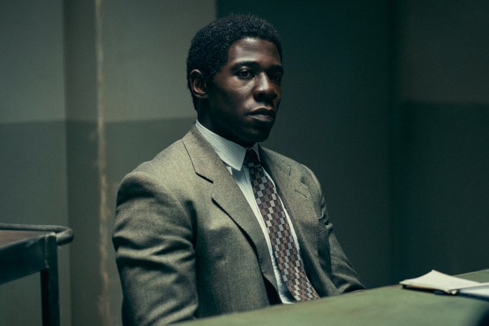Eric Season 1 McKinley Belcher III as Ledroit sitting at a table in a police station interrogation room with a stern look on his face.