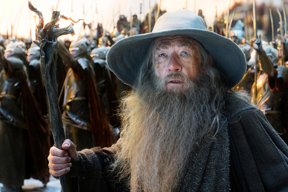 Gandalf Sir Ian McKellen as Gandalf in a robe and wizard's hat holding a staff. An army of soldiers are behind him
