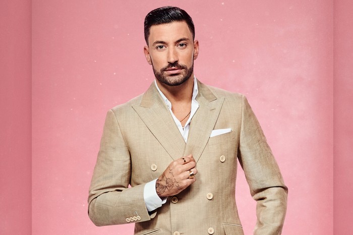 Giovanni Pernice on Strictly Come Dancing Giovanni Pernice wears a light-coloured suit and stands before a pink background
