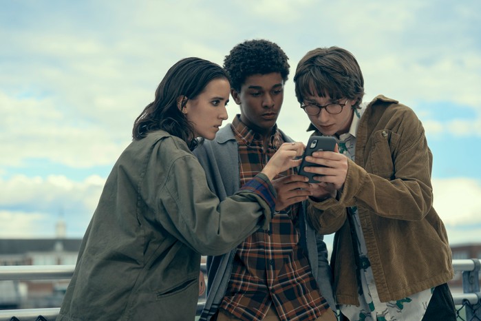 Harlan Coben’s Shelter Abby Corrigan as Ema Winslow, Jaden Michael as Mickey Bolitar and Adrian Greensmith as Arthur "Spoon" Spindell) in Harlan Coben's Shelter looking at a phone.