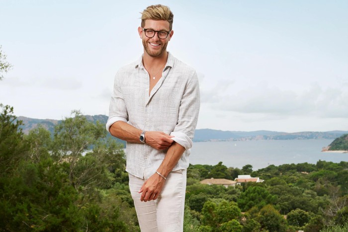 Harvey Armstrong for Made in Chelsea: Corsica Harvey Armstrong wearing a cream outfit, with trees and water in the background
