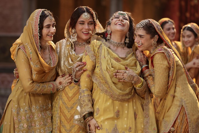 Heeramandi_Netflix_cast_2 Sanjeeda Sheikh as Waheeda, Richa Chadha as Lajjo, Manisha Koirala as Mallikajaan, Aditi Rao Hydari as Bibbo all wearing matching yellow sarees and holding each other, laughing in Heeramandi: The Diamond Bazaar.