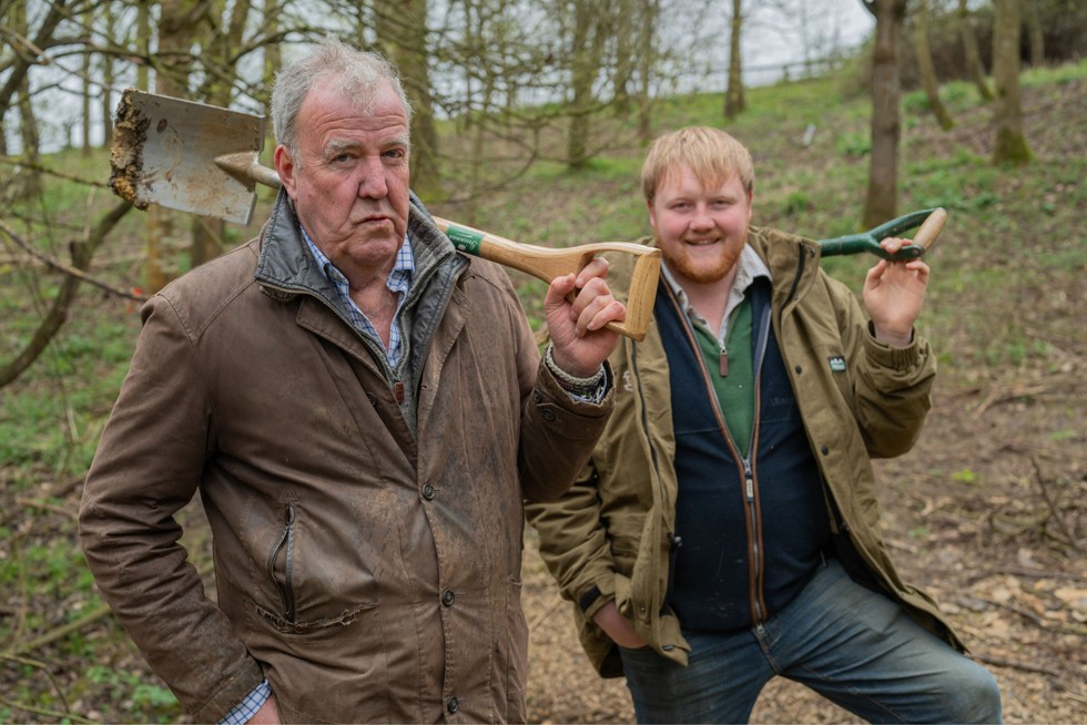 Jeremy Clarkson and Kaleb Cooper on Clarkson's Farm season 3 Jeremy Clarkson and Kaleb Cooper stood in the middle of a woodland looking ahead. They are both wearing farming clothing and have shovels resting on their shoulders.