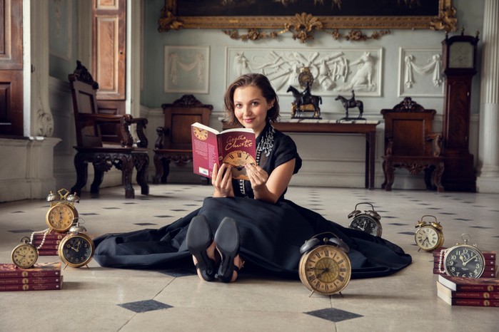 MiaMcKennaBruce_TheSevenDialsMystery_Bundle_Image1 Mia McKenna-Bruce reading The Seven Dials Mystery and sat on the floor with clocks all around her