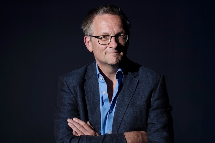 Michael Mosley Dr Michael Mosley with his arms crossed, looking at the camera in front of a dark black background.