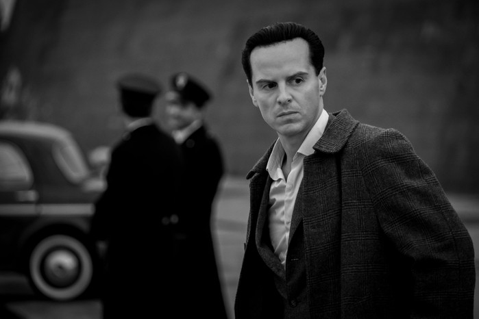 Ripley Andrew Scott as Tom Ripley with police in the background in a black-and-white still from Ripley.